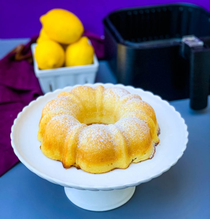 pastel de limón airfryer en un plato de pastel blanco con limones frescos
